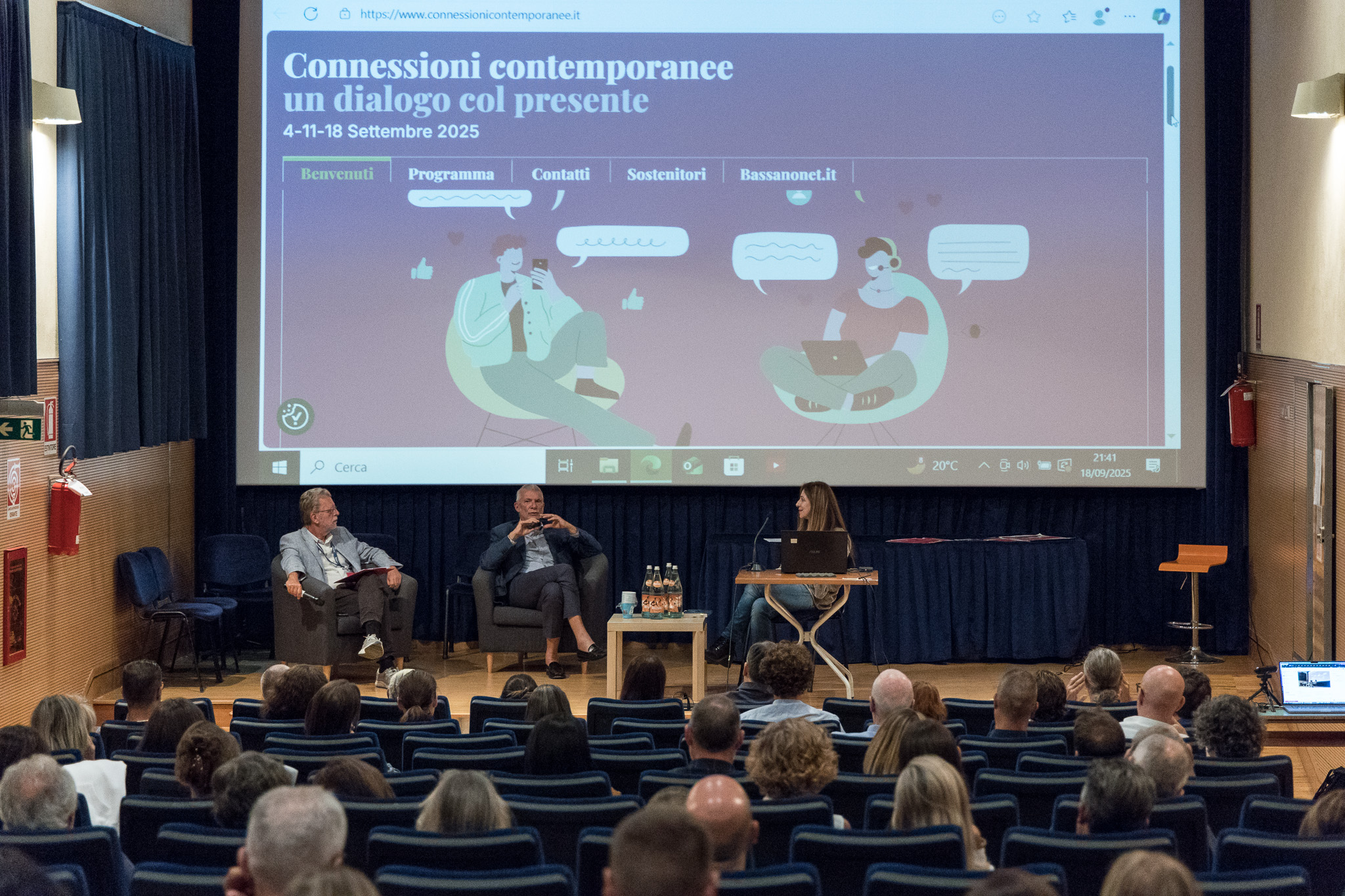 Maxischermo con il sito connessionicontemporanee.it e relatori sul palco